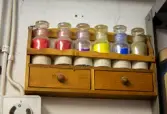 Glasburkar med pigment på trähylla 