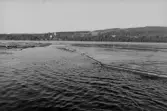 Helgumsjön. Fraktbom bogseras runt timret av en motorbåt.