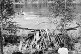 Fångsjön. Radiobåten drar ner gamla timmerupplag från stranden. Rikard Johansson kör.