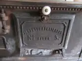 Interiör från köket i parstugan på Nygårdsgården i Bingsjö. Köket är beläget i det rum innanför förstugan som i parstugor vanligen brukar vara kammare. Troligen fick köket sin placering i samband med att byggnaden flyttades. Den stod ursprungligen på annan plats i byn men flyttades omkring 1860–1861 till nuvarande plats som då var åkermark. Vedspisen är en så kallad Faluspis, nummer 3, från Johanssons & Petterssons järngjuteri. Faluspisarna har ofta ängelmotiv på gavlarna (dock ej just denna), vilket sägs härröra från den djupt troende Pettersson som hade idén om 