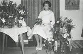 Konfirmation för Carin Gustafsson (född 1945, gift Ånskog), Nybo Gamla Riksvägen 40, okänt årtal. Carin sitter på en stol omgiven av blommor.