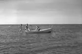 Några kvinnor sitter i en förtöjd båt ute i det långgrunda vattnet vid Skummeslövsstrand. I bakgrunden ses badande människor.