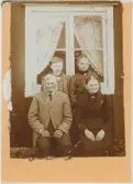 Familj sitter framför fönstret på ett bostadshus, Uppland 1905