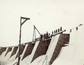 Byggandet av Älvkarleby kraftverk med arbetare uppe på den stora timmer- och stenkistan, omkring 1906 (enligt text i album).