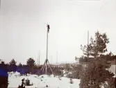 En linjemontör uppklättrad i en hög elstolpe av trä vid installation av el, vid byggandet av Älvkarleby kraftverk, omkring 1906 (enligt text i album).