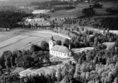 Flygbild från sydöst över Färgaryds kyrka och kyrkogård vid ån Nissan, med omgivande gårdar och odlingslandskap mellan skogspartierna.