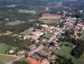 Flygbild över Hishult. Bostadshus och andra byggnader. Skog och odlingslandskap. Vägar.