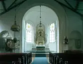 Interiörbild av Hishults kyrka. Koret med altare, altartavla och altarring. Korfönstren är rundbågade och spröjsade med cirkelmönster upptill. På ömse sidor om korvalvet ses predikstol och dopfunt.