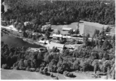 Flygbild över en fördämning i ett vattendrag med kvarnbyggnad eller sågverk. Några ytterligare bostads- och uthus ligger vid vägen.