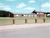 Exteriörbild av Hishults skola. Utmed Markarydsvägen står ett trådstaket mellan låga tegelpelare.