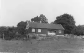 Bostadshus på en höjd i Kyrkobyn, Släp socken. Huset är timrat med en tillbyggd del till vänster i bild. Ett fasadparti är indraget under tak och putsat.