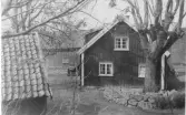 Gården Nötegång, Släp socken. Bostadshuset sett från gaveln med ekonomibyggnader. På gården står en kärra och på utsidan en cykel.