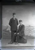 Ateljéfoto av två män i helfigur, den ena sitter. Båda bär uniform med skärmmössa med texten 