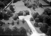 Flygbild över Susegården i Kvibille. Mangårdsbyggnad med flyglar dit en bred väg leder med damm på ena sidan och park på den andra. Bakom byggnaderna breder ägorna ut sig. Herrgården skapades av tre mantal från byn Gillarp. Susegården ägdes i början av 1600-talet av två bröder Susse, från vilken den fått sitt namn.