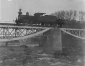 Järnvägsbron över Ätran där ett ånglok kommer farande in mot Falkenberg. I bakgrunden ses även Tullbron. Järnvägsbron anlades 1886 till Mellersta Hallands Järnväg, men ersattes med en ny 1937.
