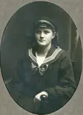 En flicka i mörk sjömansklänning och skolmössa sitter i en s.k. munkstol hos fotografen. 
Trol. Ruth Svensson (1901-1991), Alvesta, senare Stockholm.