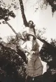 Två flickor i sommarklänningar m.m. har hoppat upp i en björk. 
Möjl. Ruth Svensson och hennes lillasyster Blenda Maria.