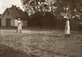 En tennismatch mellan systrarna Ruth och Blenda Svensson, trol. på skolgården till Östra Folkskolan, Alvesta. 
Till vänster syns en bod och bakom den skymtar ett bostadshus.