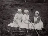Skördearbete. Tre skördearbetande kvinnor vilar sig tillsammans med sina räfsor. Bild 2 visar kvinnorna i närbild. Av frisyrerna att döma är bilden tagen på omkring 1930, och eftersom fotografen bodde i Skärte, Rolfstorp är bilden sannolikt från trakten.
