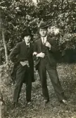 En man och en ung kvinna (utklädd till man i kostym och hög hatt) poserar för fotografen i en trädgård.
Kvinnan är Ruth Svensson.