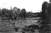 Vattendrag, Krokån vid lågvatten med gamla bron i bakgrunden. Bortom den syns kyrktornet på Knäreds kyrka. 
Text fotokopians baksida: 