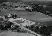 Flygfoto över Knäred med Centralskolan och omgivande villabebyggelse i fokus. Bortom åkrarna ligger Knäreds Kyrka höljd i sin trädkrans.
