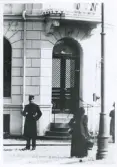En poliskonstapel har stannat till i vimlet framför ingången till dåv. Spritbolaget i hörnet Klostergatan/Norra Järnvägsgatan, ca 1913. 
Utsnitt ur större foto (BELA0073-a).