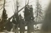 Sex kvinnor i kappa och hatt m.m., poserar för fotografen vid några stockar, med något slags ankare i bakgrunden.