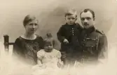 En familj bestående av en man klädd i trol. belgisk militäruniform, hans fru och två små barn, poserar hos fotografen.
Midjebild, ateljéfoto. Vykort.
På baksidan text: 